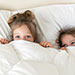 Two children covering their faces with a white comforter